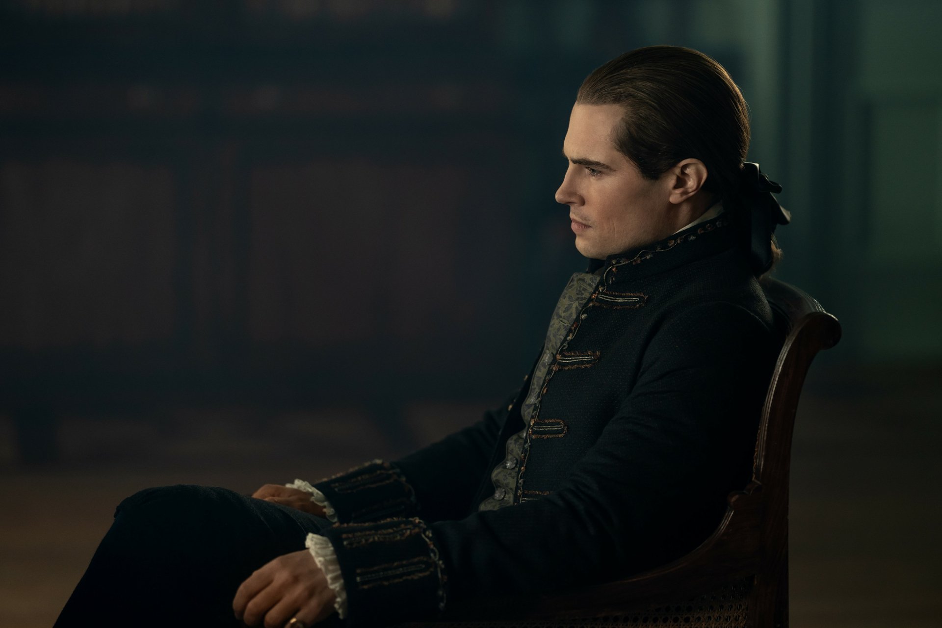 Outlander TV show 2K Quad HD PC desktop wallpaper and background: brooding 18th-century man in dark coat seated in profile against a dim, atmospheric interior.