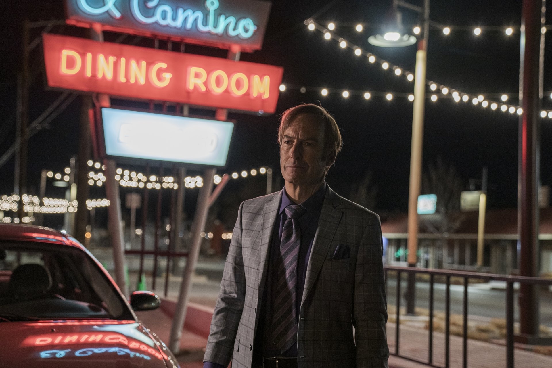 Saul Goodman, played by Bob Odenkirk in Better Call Saul, stands near a lit dining room sign at night in this 4K Ultra HD TV show desktop wallpaper.