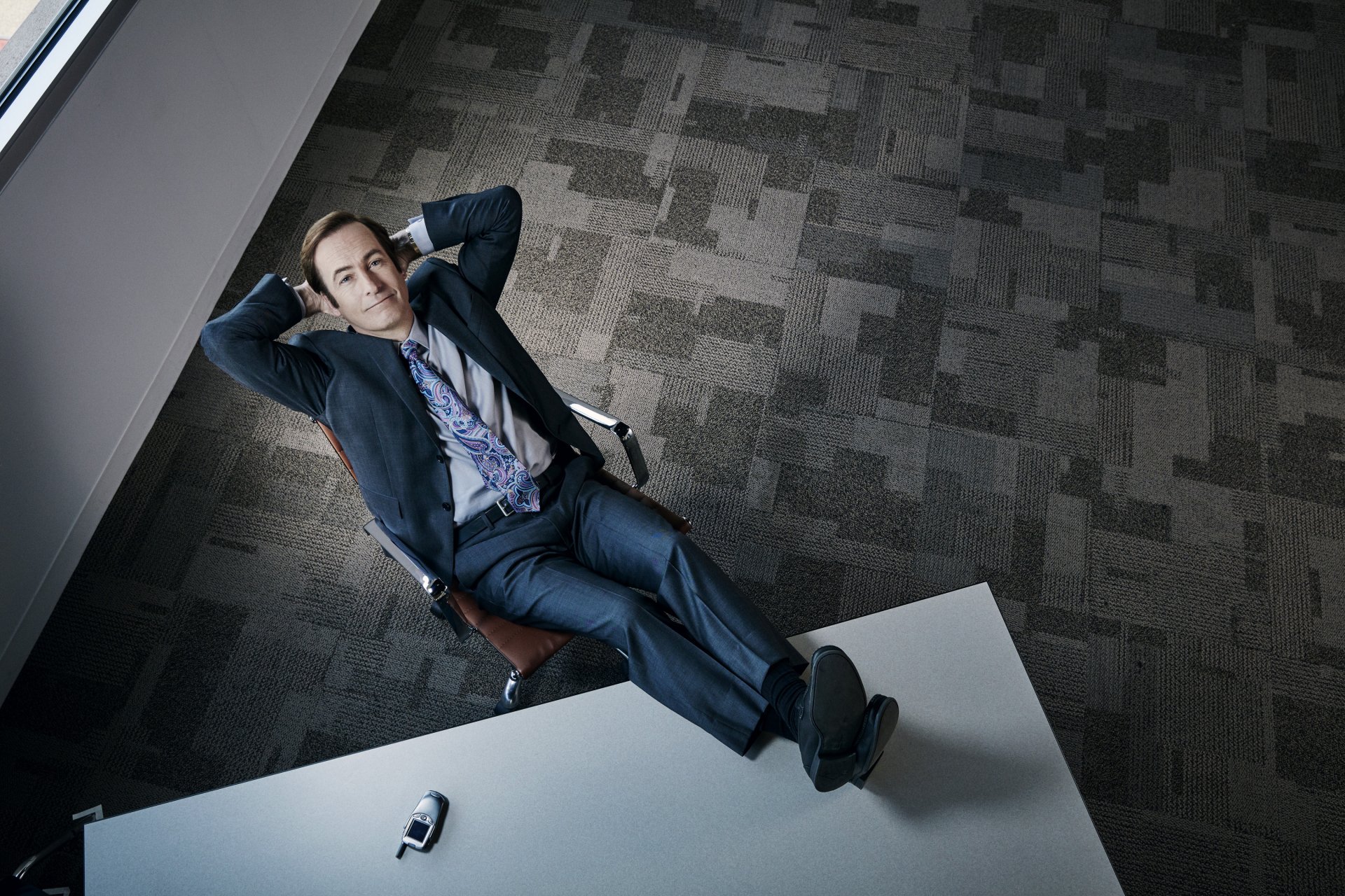 Saul Goodman (Bob Odenkirk) from the TV show Better Call Saul reclining confidently in an office, featured in an HD PC desktop wallpaper.