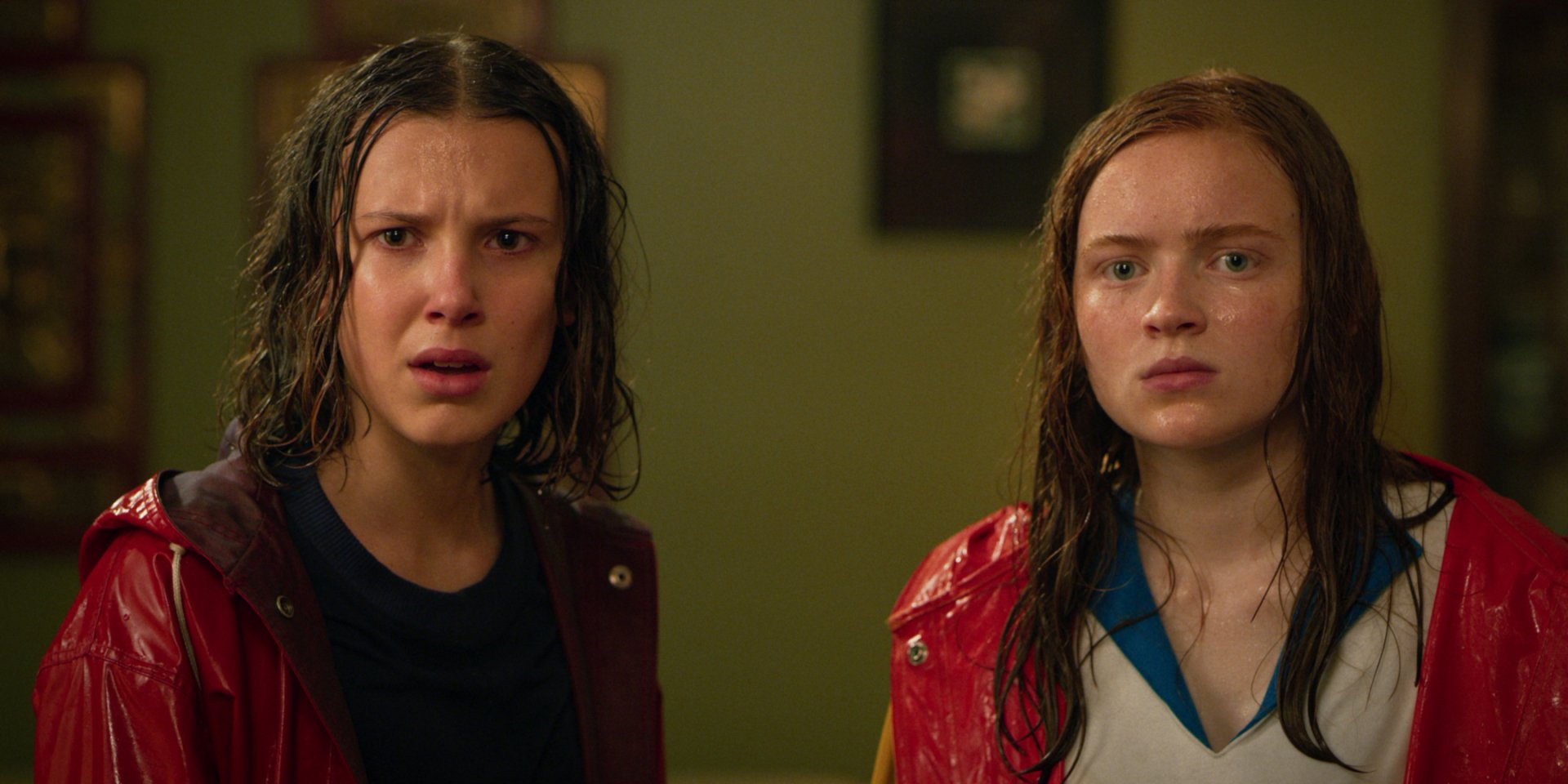 HD desktop wallpaper of Max Mayfield and Eleven from Stranger Things: two soaked teenage girls in red jackets with stunned expressions, staring ahead.