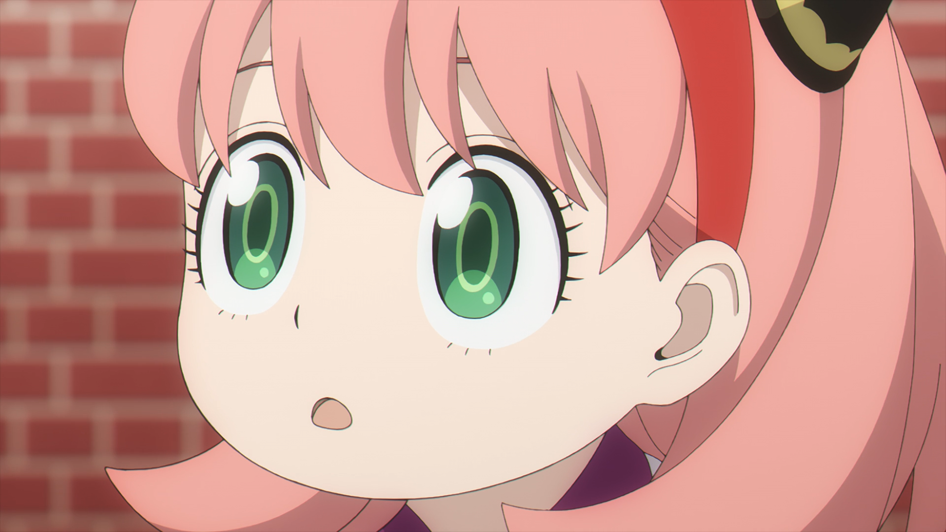HD PC desktop wallpaper: close-up anime portrait of Anya Forger from Spy x Family, pink hair and wide green eyes against a brick background.