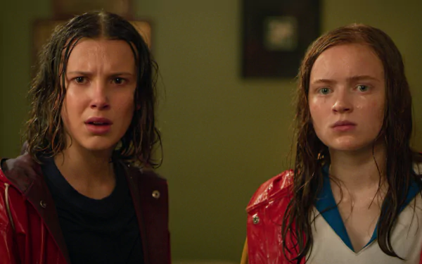 HD desktop wallpaper of Max Mayfield and Eleven from Stranger Things: two soaked teenage girls in red jackets with stunned expressions, staring ahead.