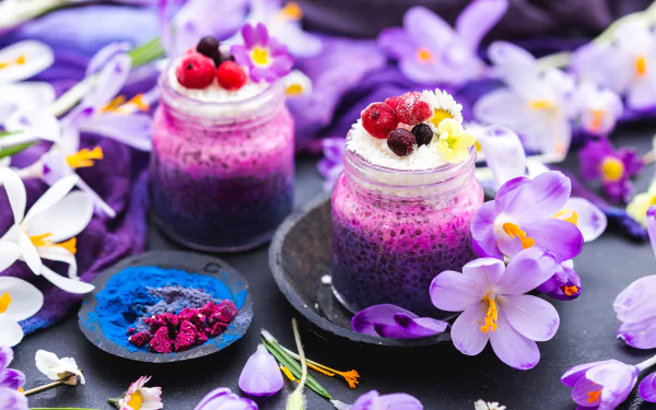 Vibrant food dessert: two purple berry chia jars topped with cream and berries, surrounded by purple flowers — 4K Ultra HD PC desktop wallpaper background.