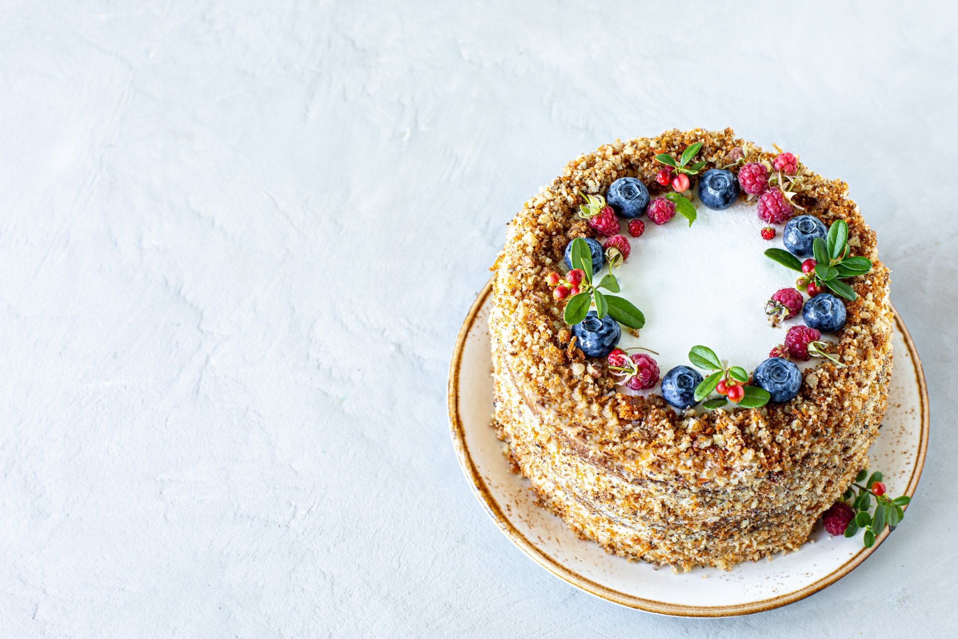 4K Ultra HD PC desktop wallpaper of food: a layered nut-crusted cake with smooth white frosting, topped with berries and herbs, on a plate against a pale textured background.