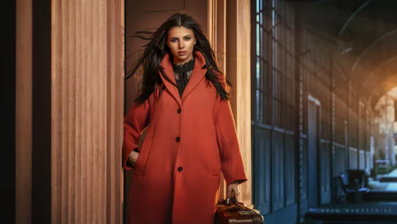 HD PC desktop wallpaper of a woman model in a red coat walking through an elegant columned corridor, carrying a vintage suitcase against a moody, cinematic background.