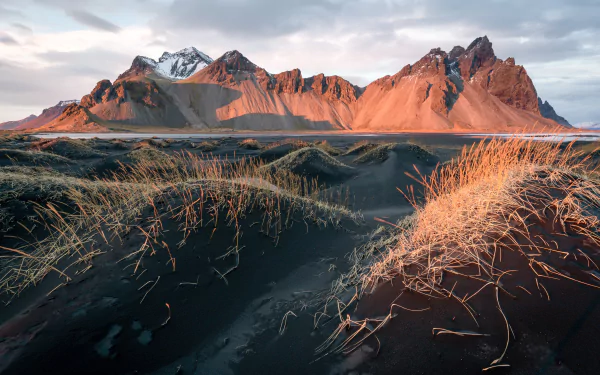 4K Ultra HD desktop wallpaper showcasing the rugged Vestrahorn mountains bathed in warm light, with foreground dunes and grasses under a cloudy sky.