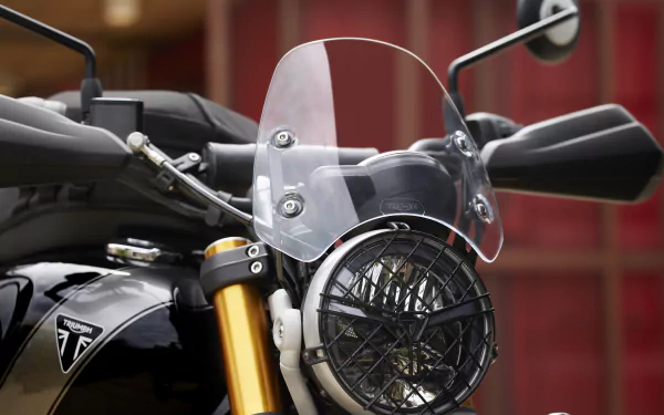 Close-up of a Triumph Scrambler 400 X motorcycle, highlighting its stylish headlight and protective windshield. This vibrant image serves as an HD desktop wallpaper and background.