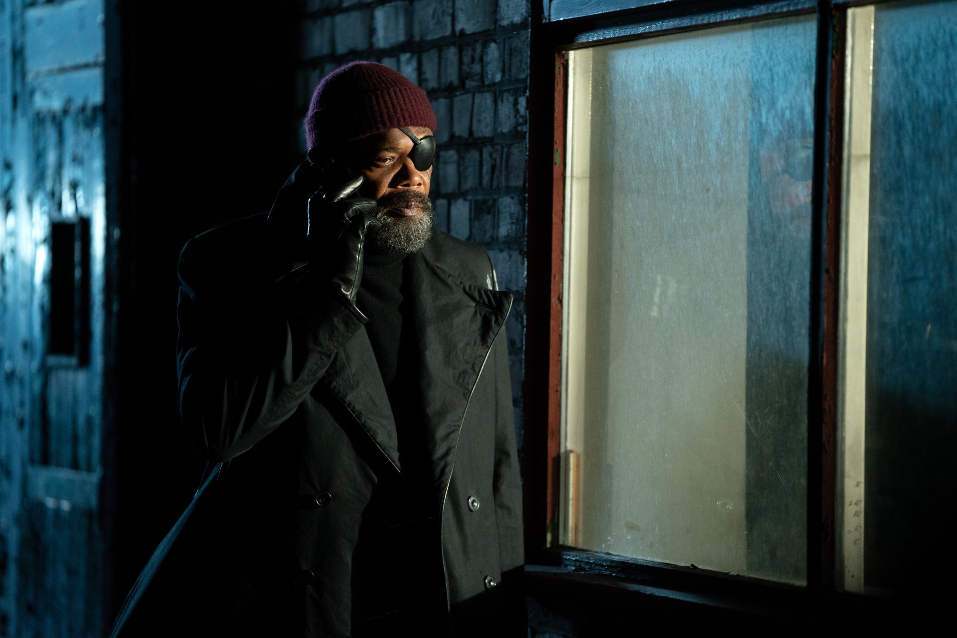 HD desktop wallpaper from the TV show Secret Invasion featuring the character Nick Fury, portrayed by Samuel L. Jackson, using a phone in a dimly lit environment.