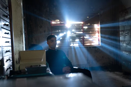 HD wallpaper of Secret Invasion theme with a mysterious character seated at a desk in a dimly lit room with rays of light streaming through the window.