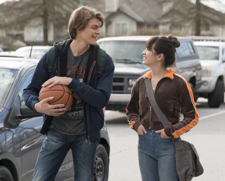 Two smiling teenagers, a boy holding a basketball and a girl with a backpack, engaging in a friendly conversation on a school campus, available as Prom Pact HD desktop wallpaper and background.