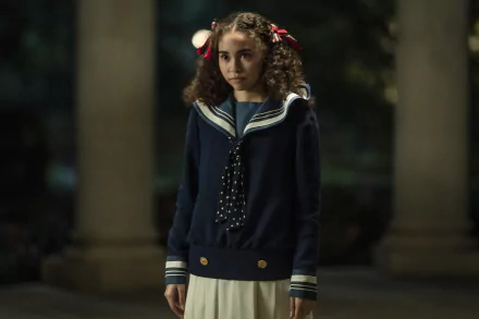 HD wallpaper featuring a character from Interview with the Vampire series portrayed by actress Bailey Bass, standing with a solemn expression in a vintage-style school uniform against a dimly lit, atmospheric backdrop.