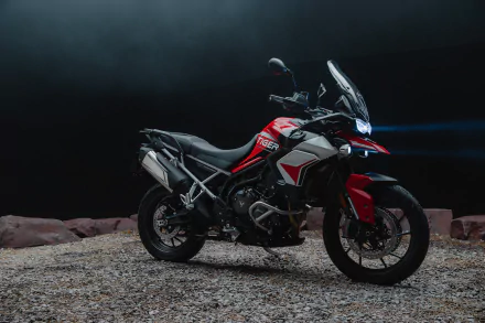 Triumph Tiger 900 GT Aragón showcased in a striking HD wallpaper. The motorcycle stands on gravel with dramatic lighting, highlighting its sleek design and features.