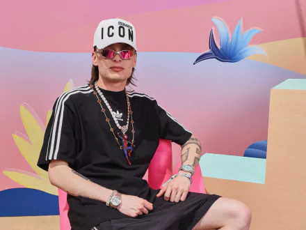 Stylish person wearing 'ICON' cap and sports attire posing in front of a colorful abstract backdrop - Peso Pluma themed HD desktop wallpaper and background.