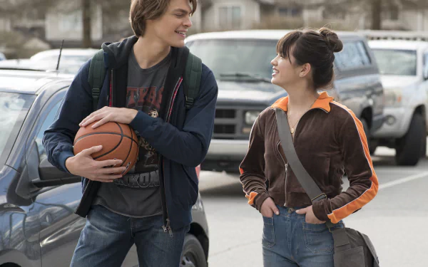 Two smiling teenagers, a boy holding a basketball and a girl with a backpack, engaging in a friendly conversation on a school campus, available as Prom Pact HD desktop wallpaper and background.
