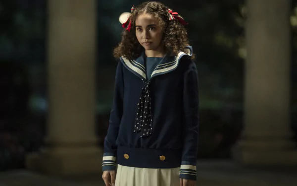 HD wallpaper featuring a character from Interview with the Vampire series portrayed by actress Bailey Bass, standing with a solemn expression in a vintage-style school uniform against a dimly lit, atmospheric backdrop.