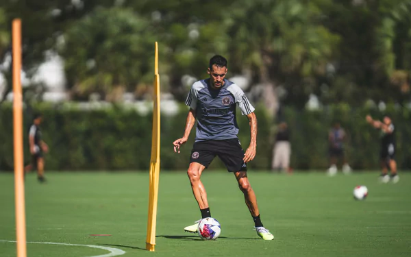 HD wallpaper of Sergio Busquets training with Inter Miami CF, focusing on dribbling around yellow poles on a lush green field.