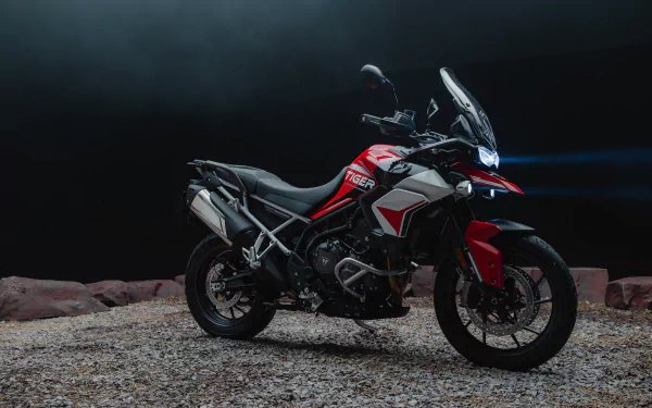 Triumph Tiger 900 GT Aragón showcased in a striking HD wallpaper. The motorcycle stands on gravel with dramatic lighting, highlighting its sleek design and features.