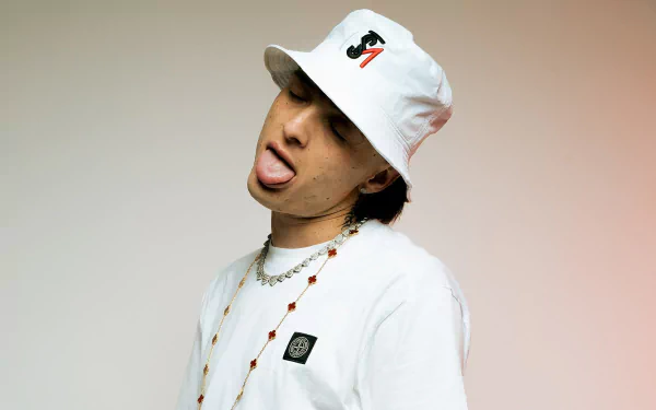 A vibrant HD desktop wallpaper featuring Peso Pluma, a Mexican musician, playfully posing in a white hat and t-shirt, showcasing his unique style and charisma.