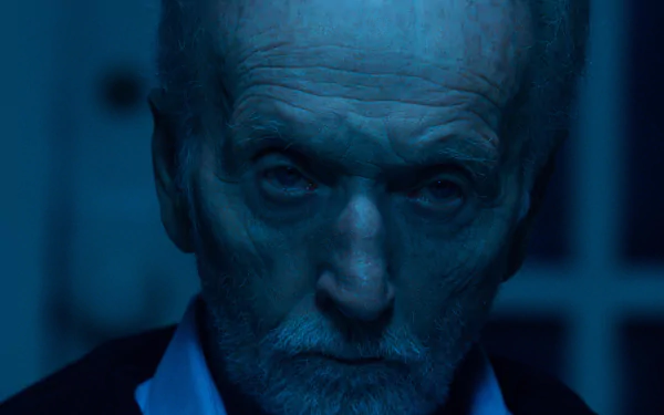 A close-up of Tobin Bell from the movie Saw X, featuring intense lighting that highlights his expression. This HD desktop wallpaper captures a chilling atmosphere.