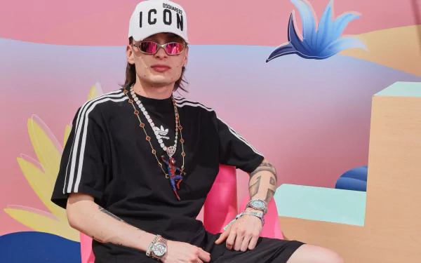 Stylish person wearing 'ICON' cap and sports attire posing in front of a colorful abstract backdrop - Peso Pluma themed HD desktop wallpaper and background.