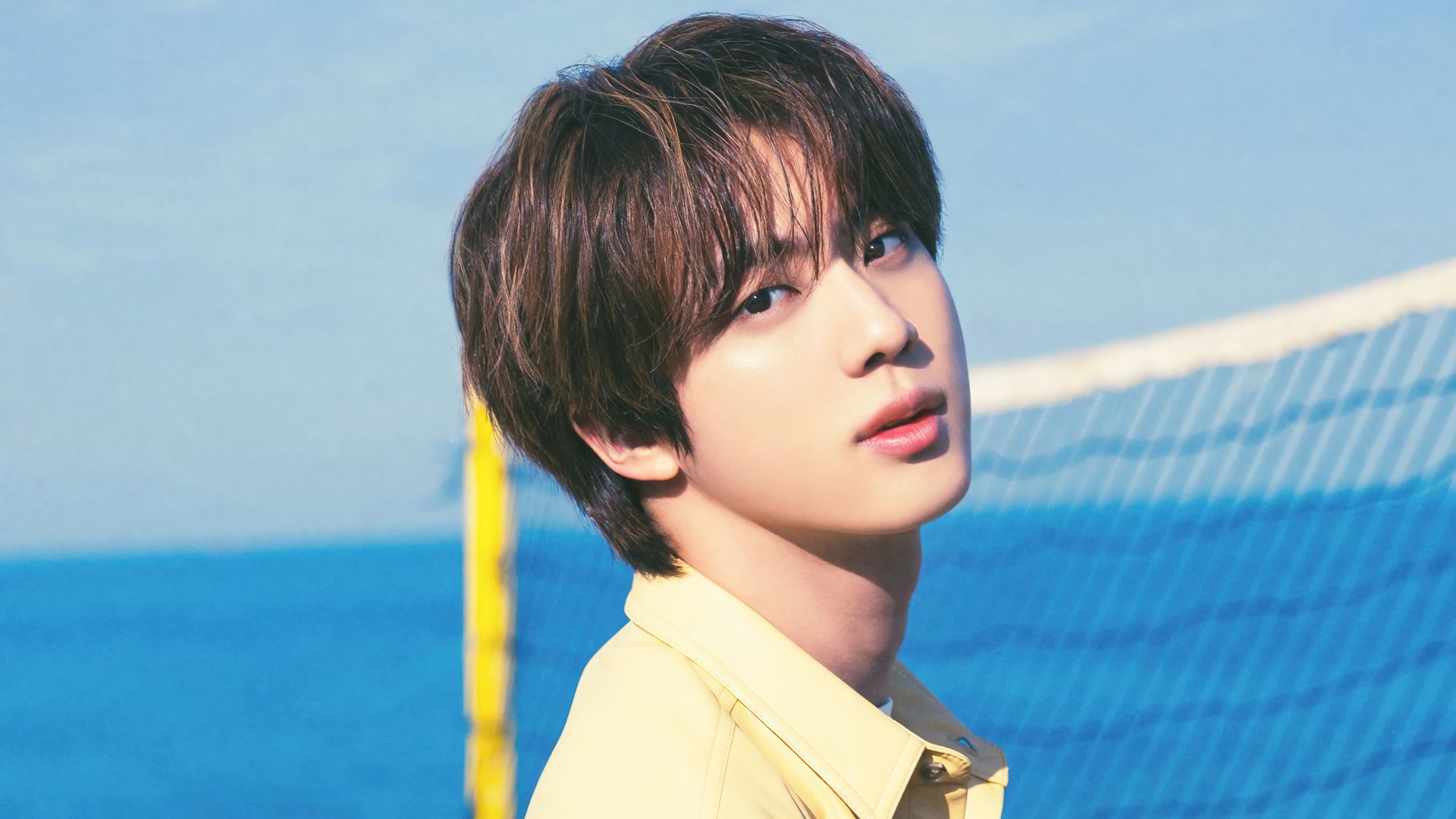 A serene HD desktop wallpaper featuring Kim Seok-jin from BTS, capturing his charming look against a vibrant blue ocean background.