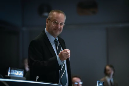 Man in a suit speaking at a conference in a For All Mankind themed HD desktop wallpaper.