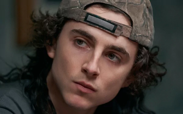 High-definition desktop wallpaper featuring a close-up of a young man with curly hair wearing a camouflage cap, providing a cinematic and moody background vibe.