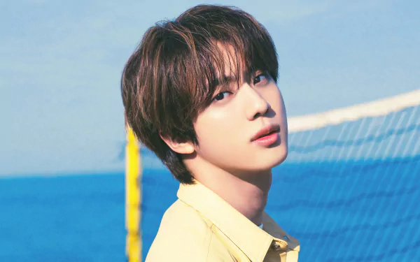 A serene HD desktop wallpaper featuring Kim Seok-jin from BTS, capturing his charming look against a vibrant blue ocean background.