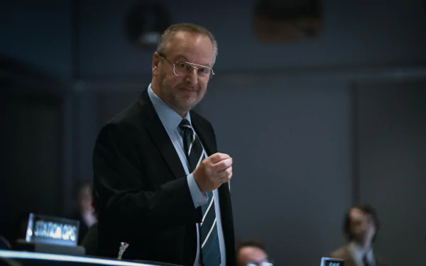 Man in a suit speaking at a conference in a For All Mankind themed HD desktop wallpaper.