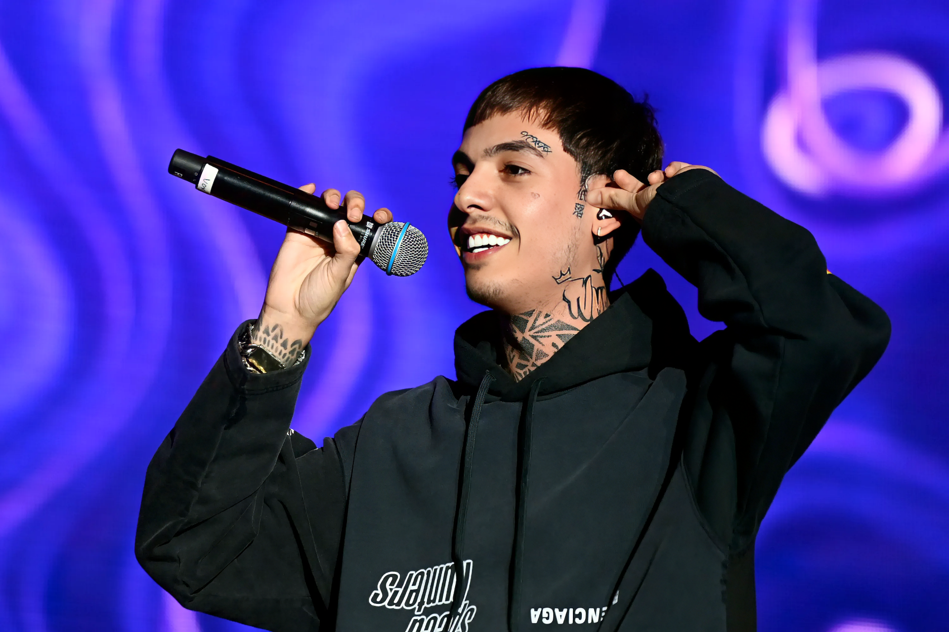 HD desktop wallpaper of a performer holding a microphone on stage with a vibrant purple background.