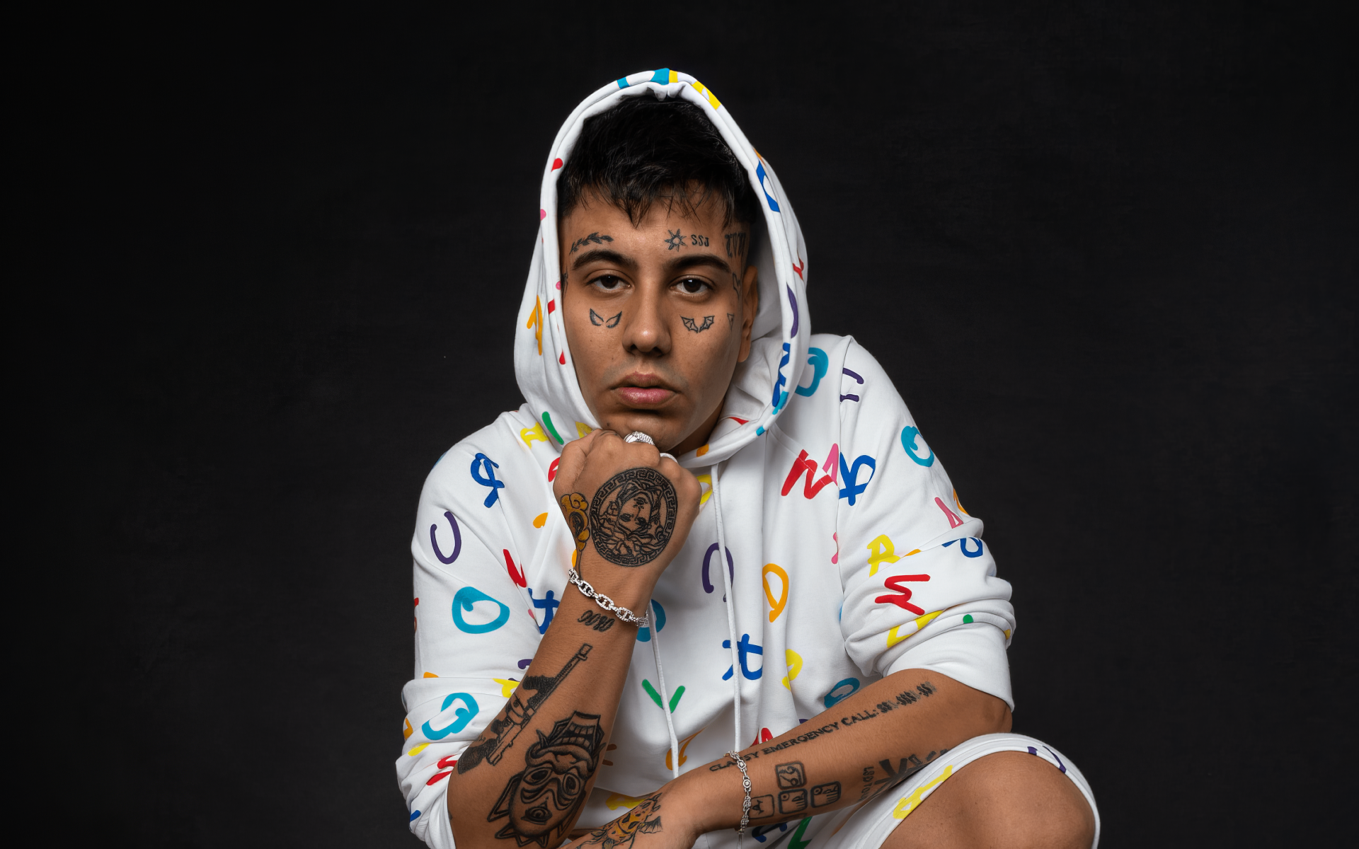 Duki poses confidently in a colorful hoodie, showcasing his tattoos against a dark background. This HD image serves as an eye-catching music-themed desktop wallpaper.