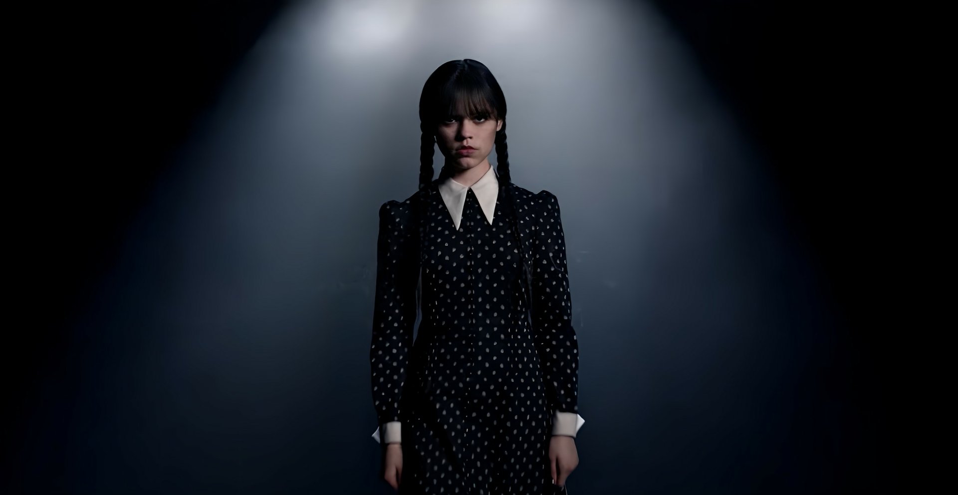 HD desktop wallpaper featuring Wednesday Addams from the TV show Wednesday, standing in a spotlight against a dark background.