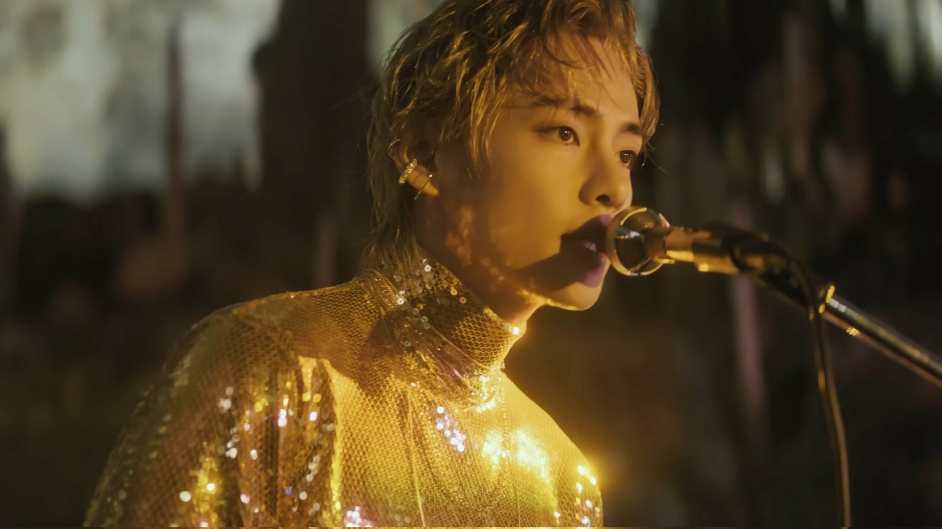 HD PC desktop wallpaper featuring a close-up of a K-pop idol in a sparkling outfit, singing into a microphone with a warm, golden glow.