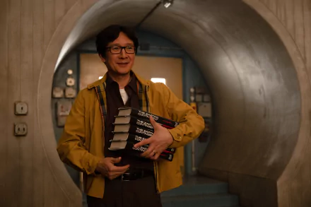 Ke Huy Quan smiles while holding books in a scene from the TV show Loki. The image serves as a vibrant HD desktop wallpaper and background.