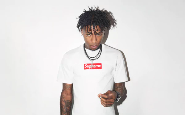 Music artist standing against a white background wearing a Supreme shirt, suitable as an HD desktop wallpaper and background for fans of YoungBoy Never Broke Again.