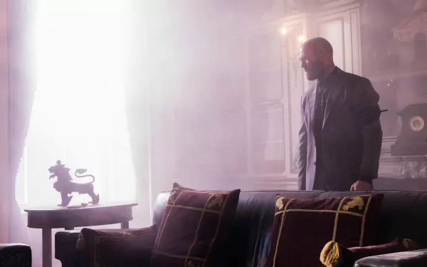 A man stands thoughtfully in an elegant, sunlit room featuring ornate furniture and dramatic shadows, inspired by the movie The Beekeeper - a high-definition desktop wallpaper.