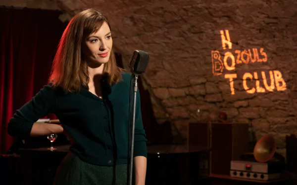 A young woman stands confidently at a microphone in a cozy club setting, with warm lighting and a stone wall backdrop, capturing a moment from the TV show Monsieur Spade.