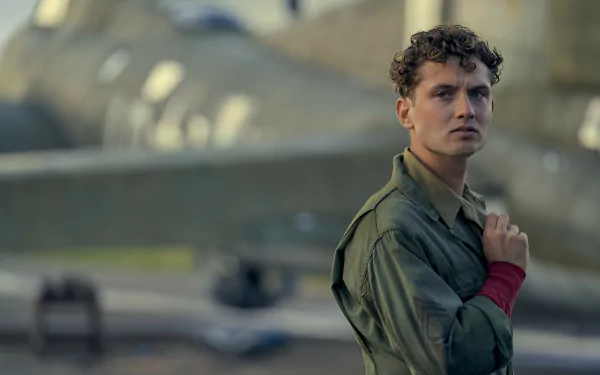 HD wallpaper featuring a scene from the TV show Masters of the Air with a focused actor in military attire standing in front of a historical airplane.