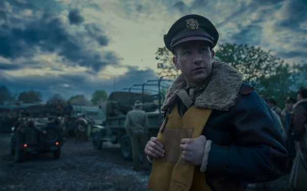 HD wallpaper of a scene from the TV show Masters of the Air featuring an officer in uniform with military vehicles in the background.