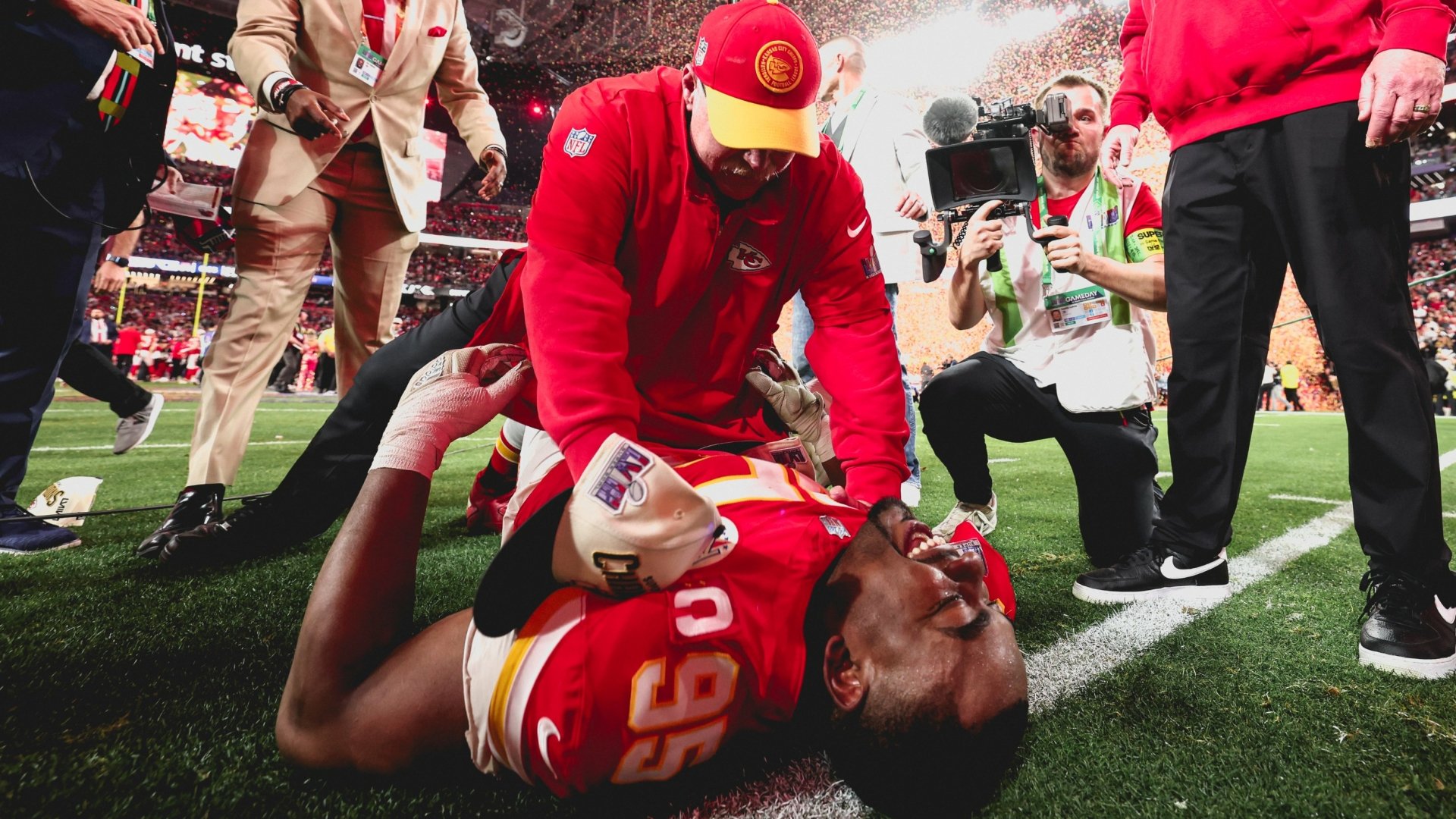A Kansas City Chiefs player lies on the field as a coach attends to him, capturing the intense moment of NFL action during the Super Bowl. High-definition sports wallpaper.