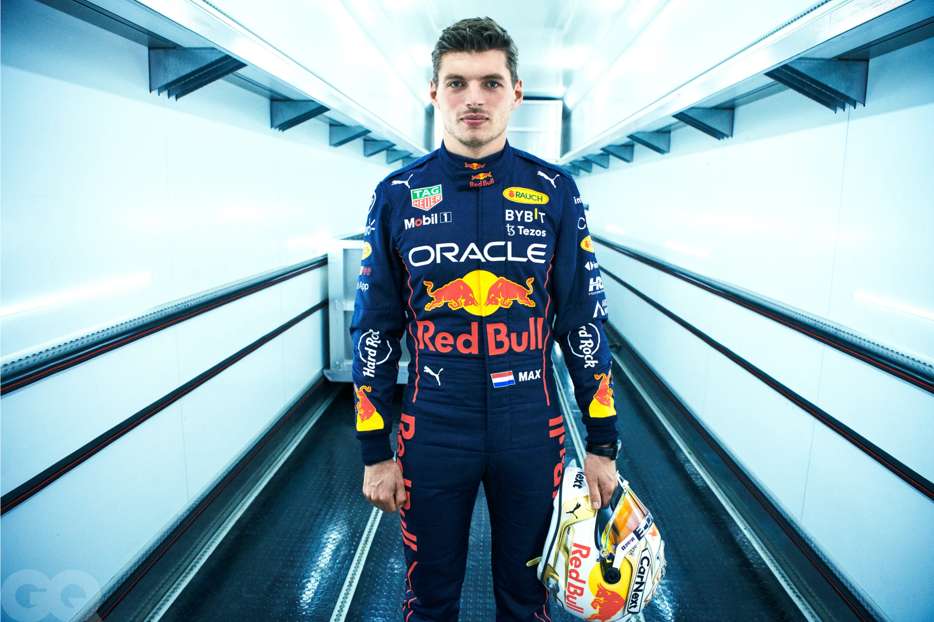 HD wallpaper of an F1 racer in full gear standing confidently in a futuristic corridor, representing the speed and precision of elite motorsports.