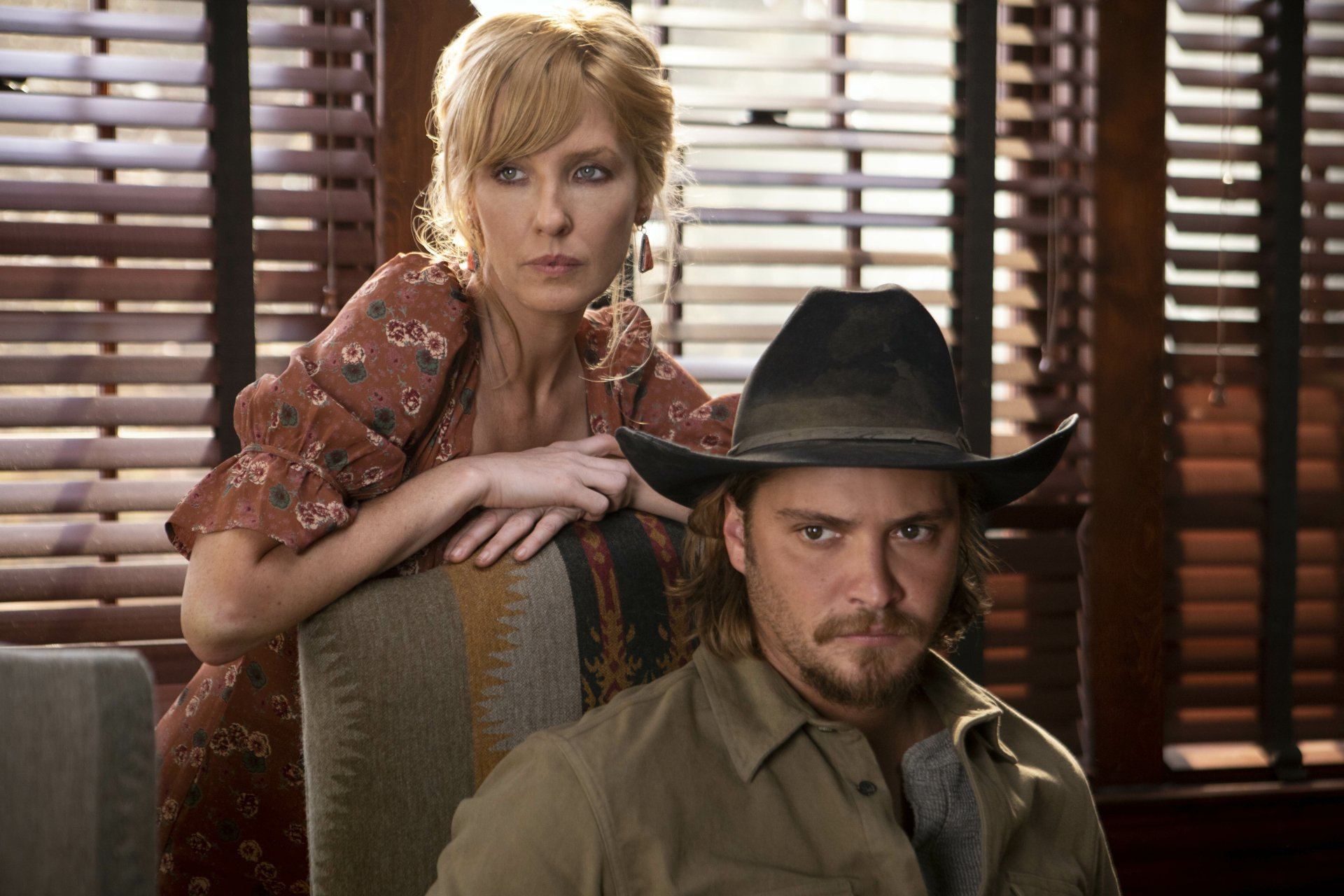 HD desktop wallpaper featuring two characters from the television show Yellowstone, with a woman standing behind a seated man wearing a cowboy hat.