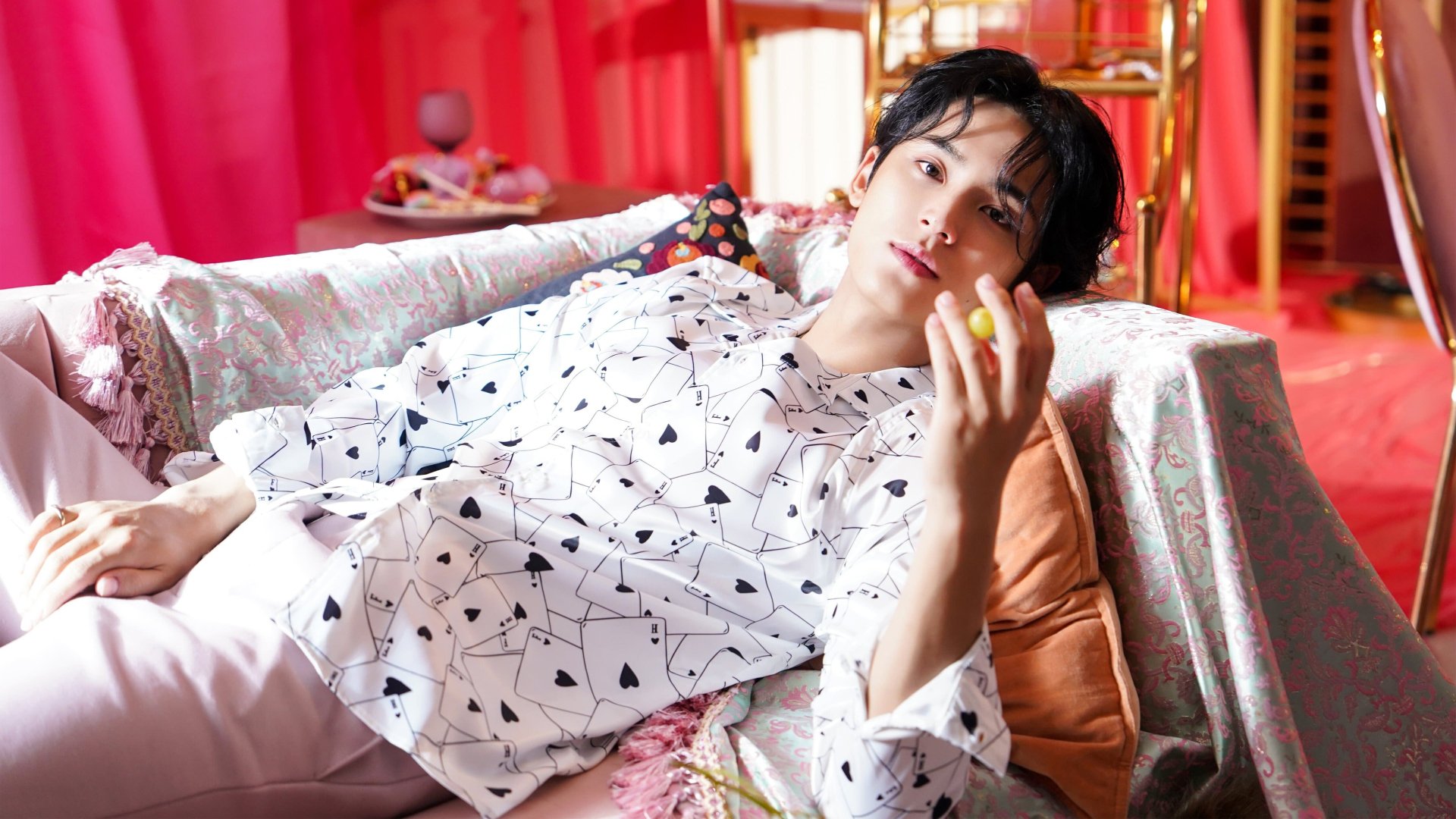 A stunning HD desktop wallpaper featuring Jimin from BTS, lounging on a colorful couch, exuding charisma in a patterned outfit against a vibrant pink backdrop.