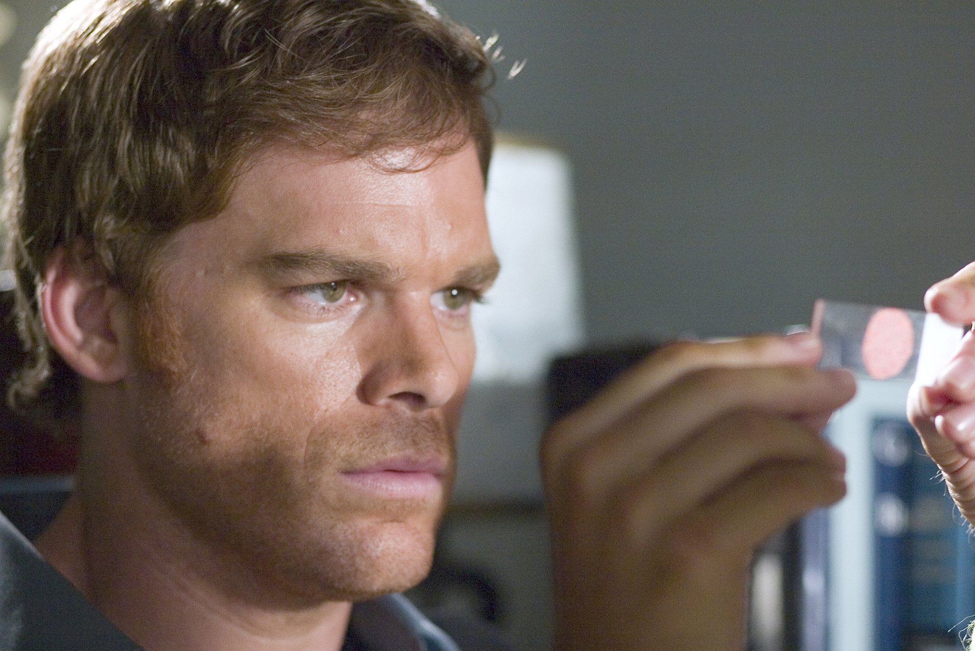 High-definition desktop wallpaper featuring a focused character from the TV show Dexter analyzing evidence.