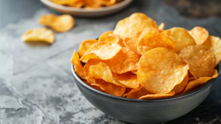 A close-up view of golden crispy potato chips in a black bowl, with a textured gray background, creating an inviting and appetizing HD desktop wallpaper.