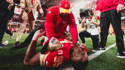 A Kansas City Chiefs player lies on the field as a coach attends to him, capturing the intense moment of NFL action during the Super Bowl. High-definition sports wallpaper.