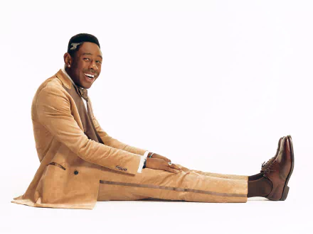 HD desktop wallpaper featuring a smiling man in a stylish beige suit, embodying the music and spirit of rapper Tyler, the Creator, against a white background.