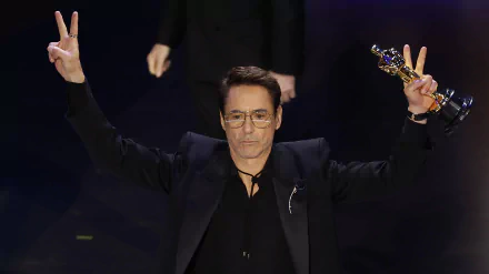 Celebratory figure at the Academy Awards holding an Oscar statuette with victory gestures in a HD wallpaper background.