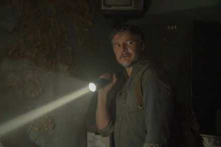 A gripping scene from The Last Of Us features Joel, played by Pedro Pascal, holding a flashlight in a dimly lit setting, evoking a sense of tension and survival.