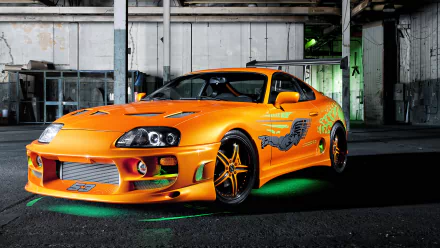 HD wallpaper of a vibrant orange Toyota Supra with stylish decals, showcased in an industrial setting.